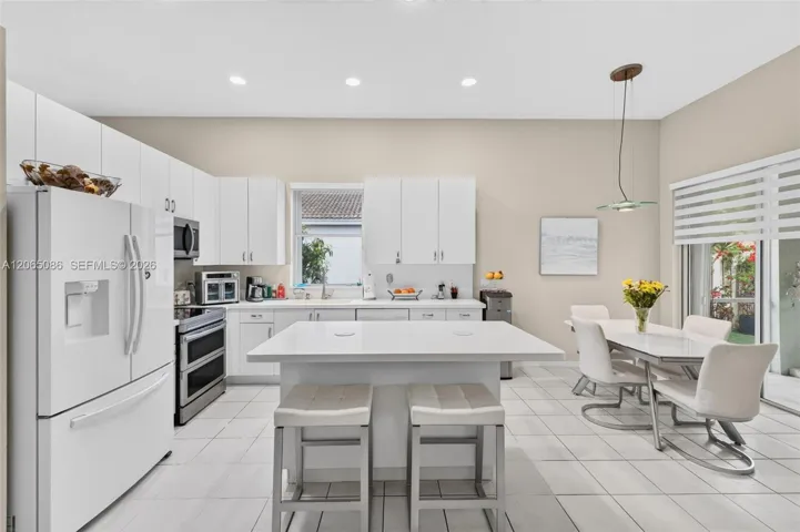 White, bright, open concept kitchen with solid surface counters and roller shades - views looking out to the giant screened, roofed and tiled patio