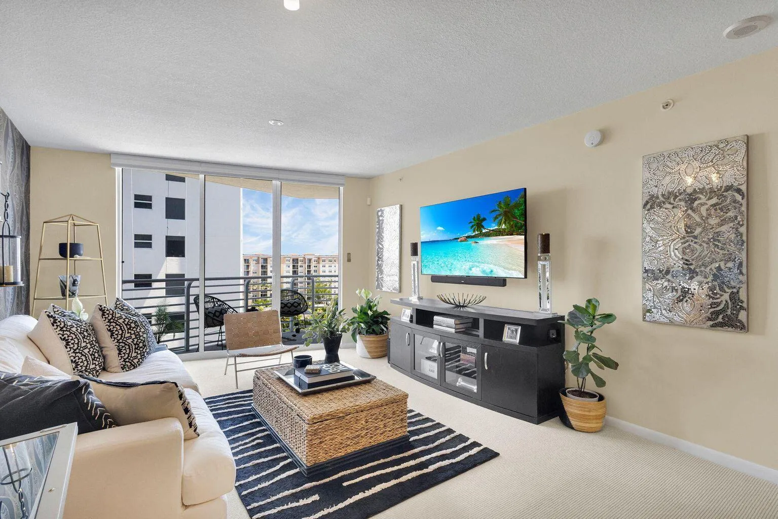 Spacious living area featuring large sliding glass doors leading to a private balcony, light-toned wall paint, and light-colored carpeting