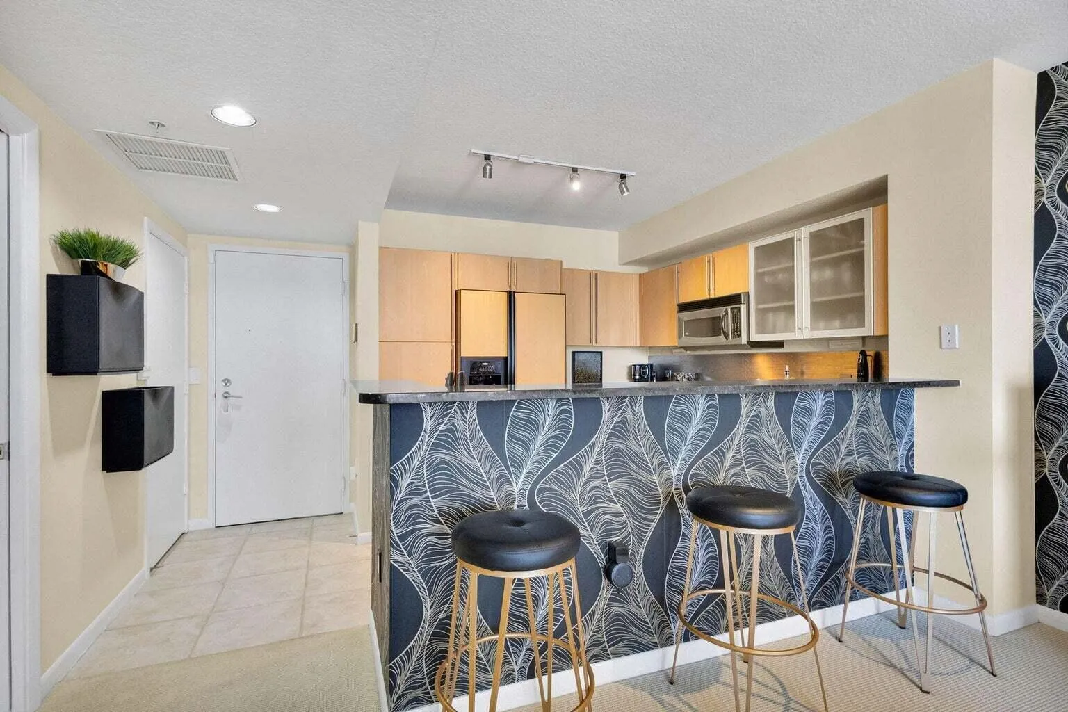 Kitchen with light wood cabinetry, stainless steel microwave, and glass-front upper cabinets