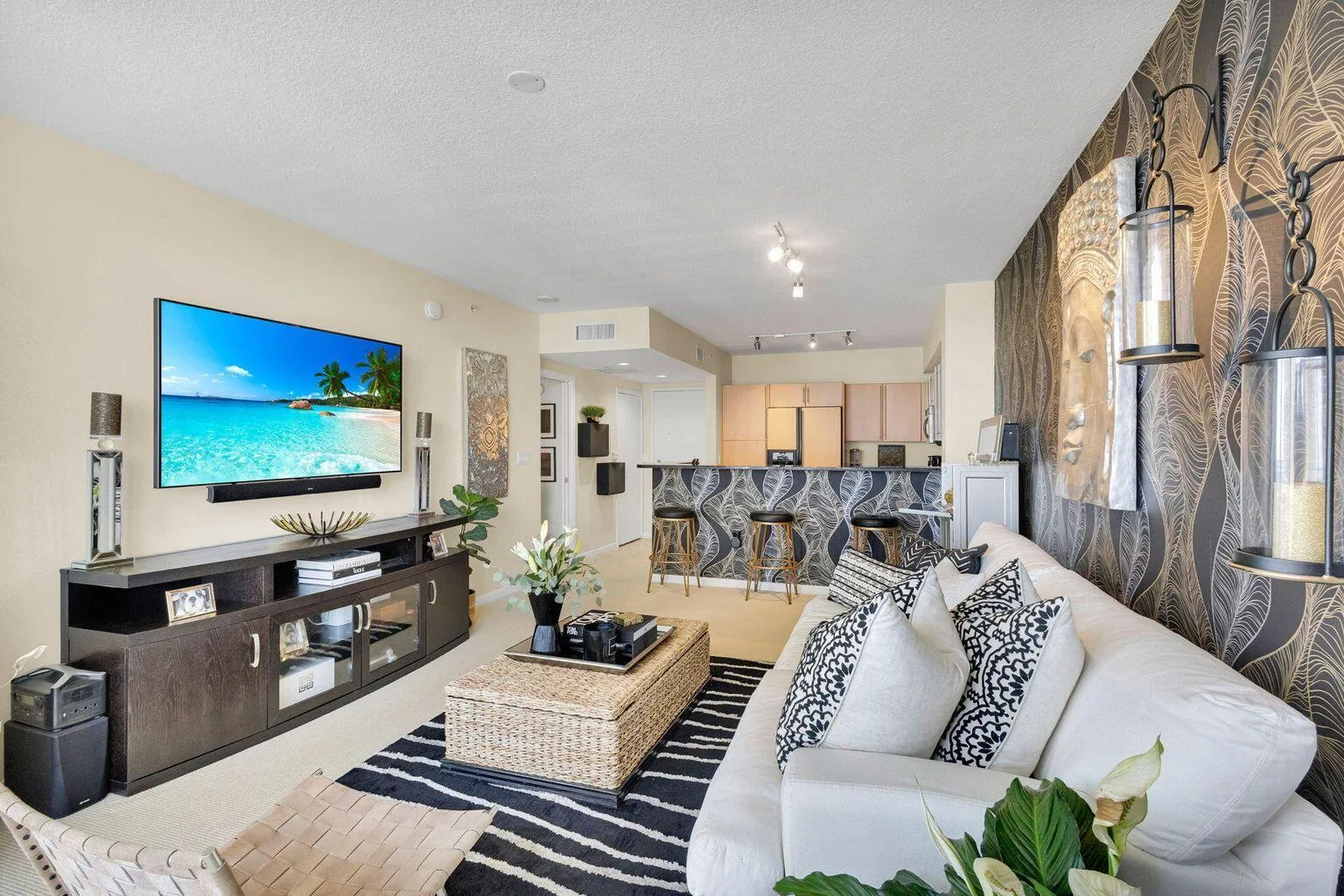 Open concept living area featuring a neutral color palette, accent wall with decorative sconces, recessed lighting, and a breakfast bar with countertop seating