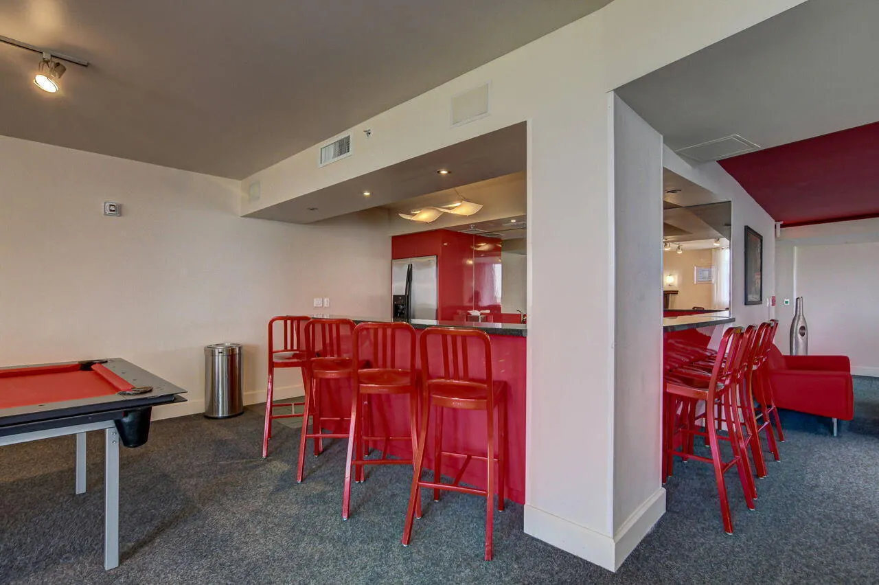 Recreational space featuring a built-in bar with red cabinetry, a mirrored backsplash, and overhead lighting