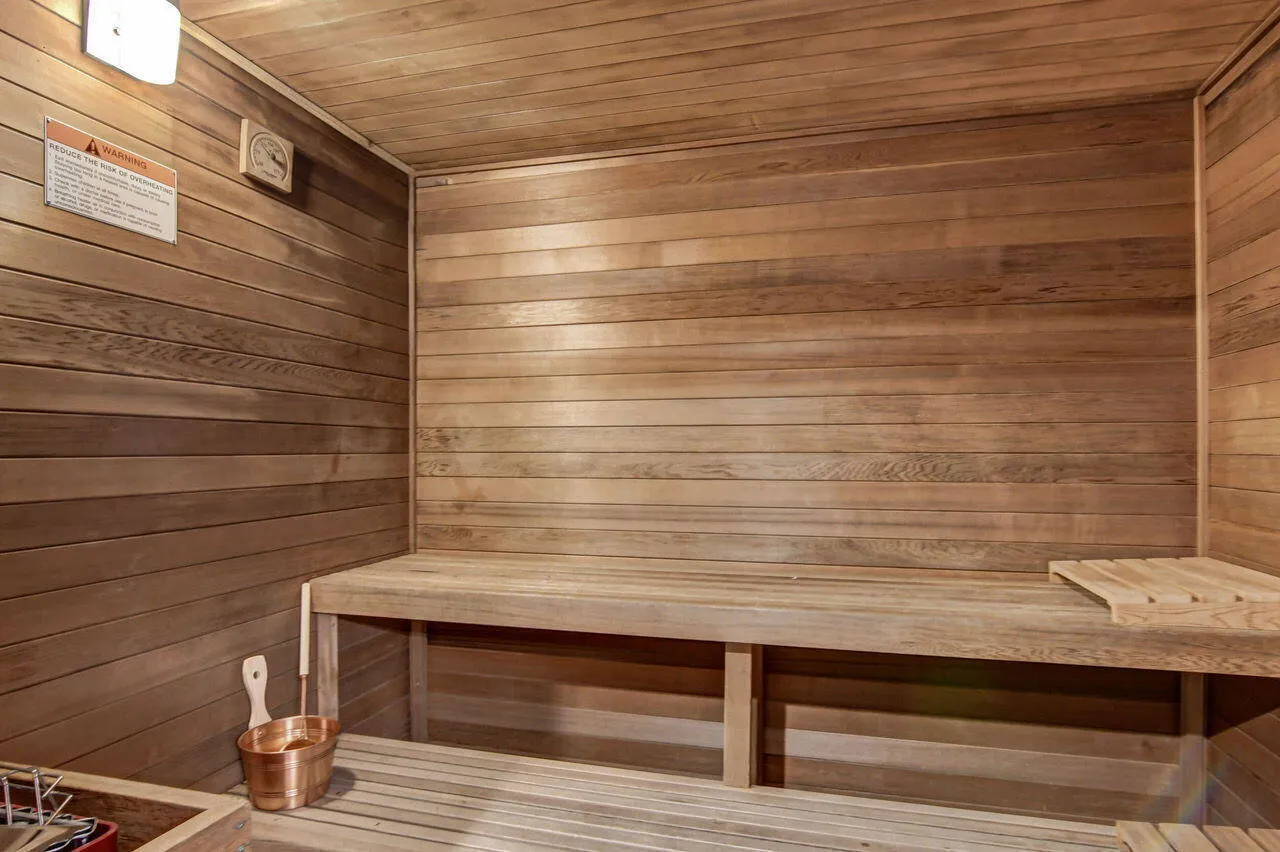 Wood-paneled sauna featuring built-in bench seating, slatted wood flooring, and a wall-mounted temperature gauge