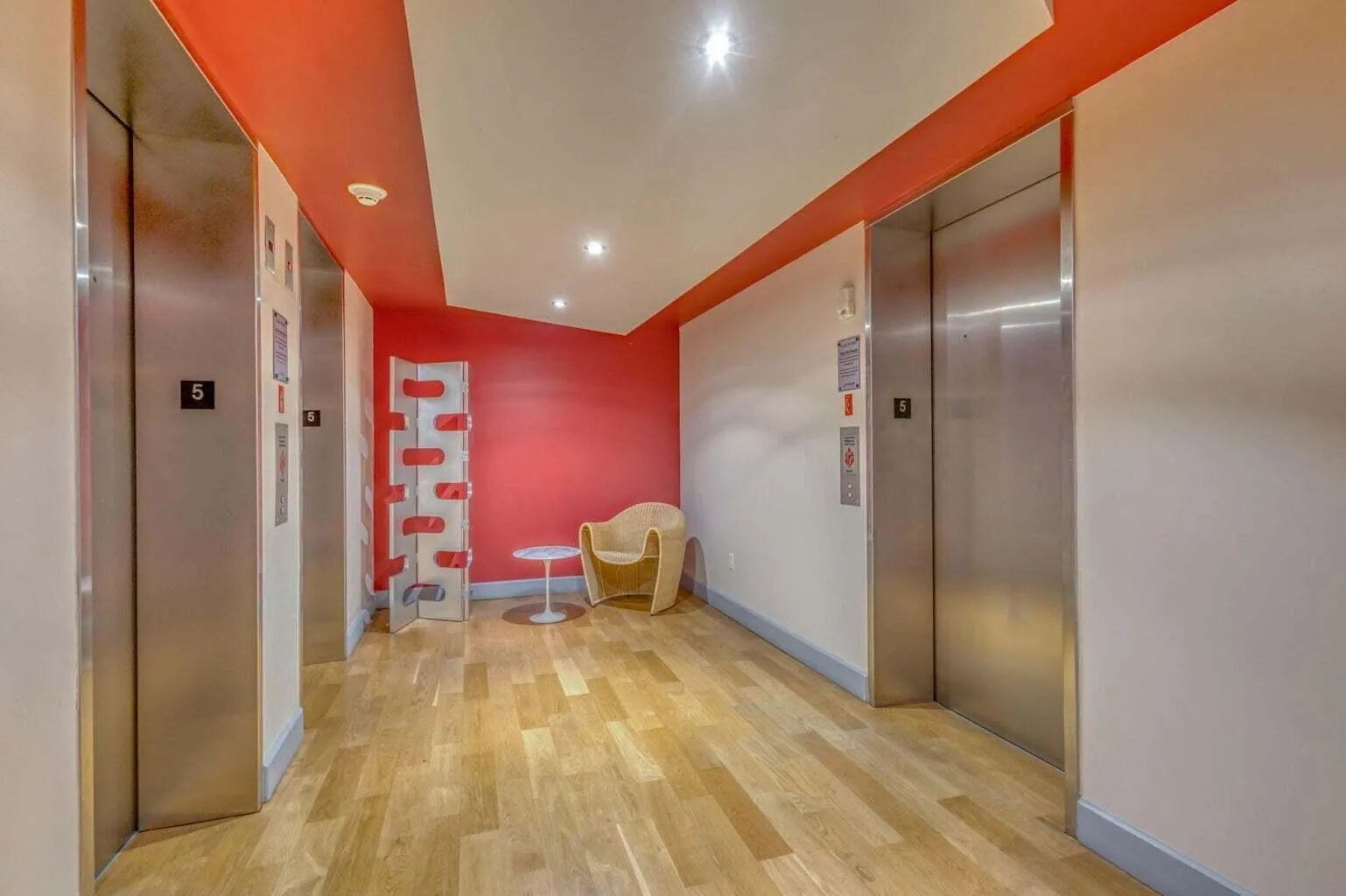Elevator lobby featuring two stainless steel elevators, overhead recessed lighting, wood-finish flooring, and a contemporary red accent wall