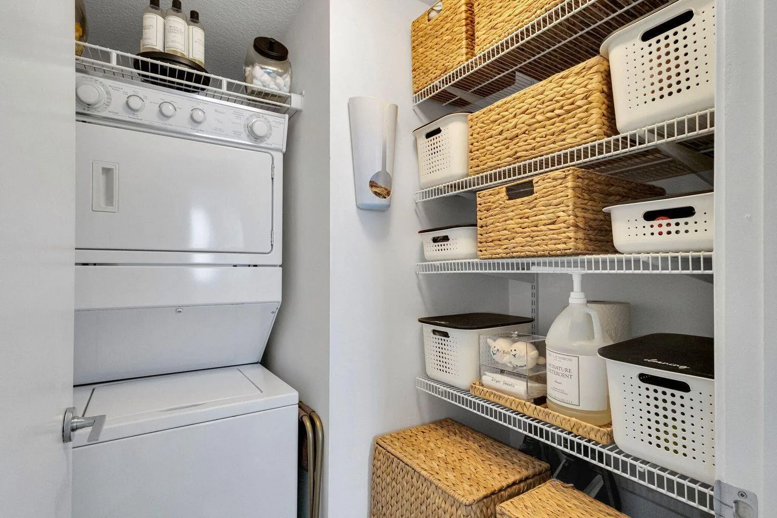 Dedicated laundry area featuring a stacked white washer and dryer, adjacent wire shelving system, and white wall finishes