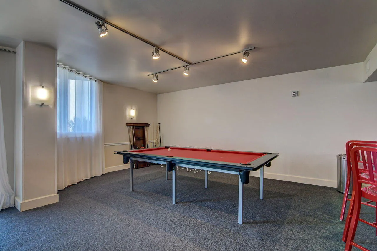 Recreation space featuring a billiard table with red felt, track lighting, wall sconces, and a window with sheer white curtains
