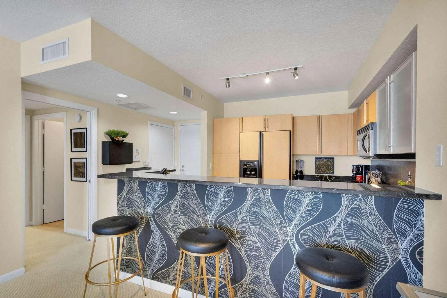 Kitchen featuring a breakfast bar with a patterned facade, granite countertop, light wood cabinetry, and stainless steel appliances