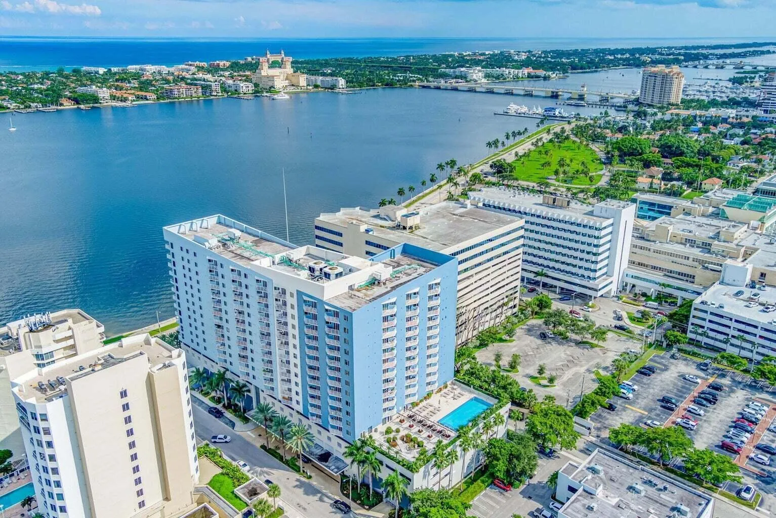 Waterfront high-rise building featuring a rooftop pool deck, multiple balconies, and integrated street-level commercial spaces