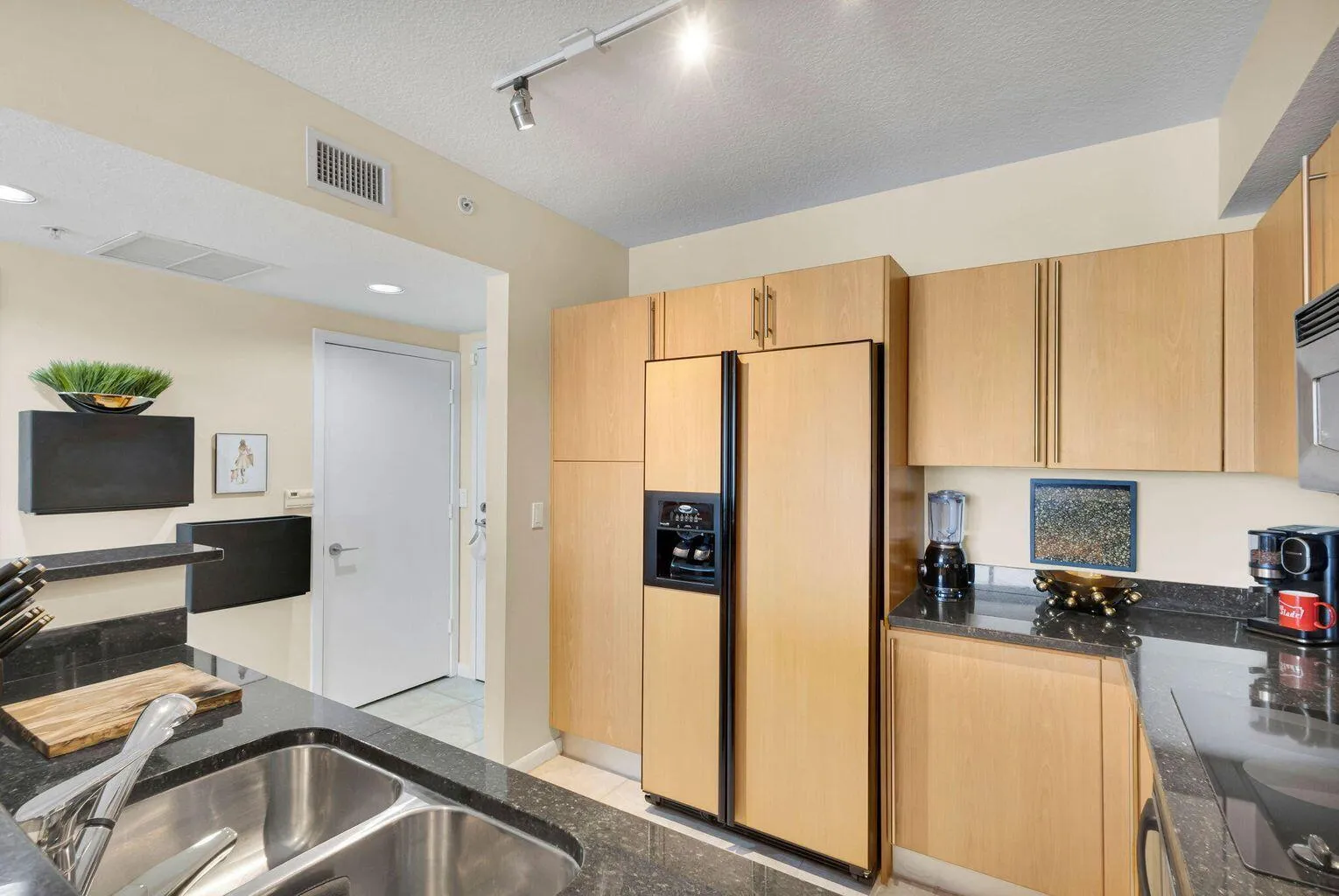Kitchen featuring dark stone countertops, undermount double basin sink, and light wood-finish cabinetry