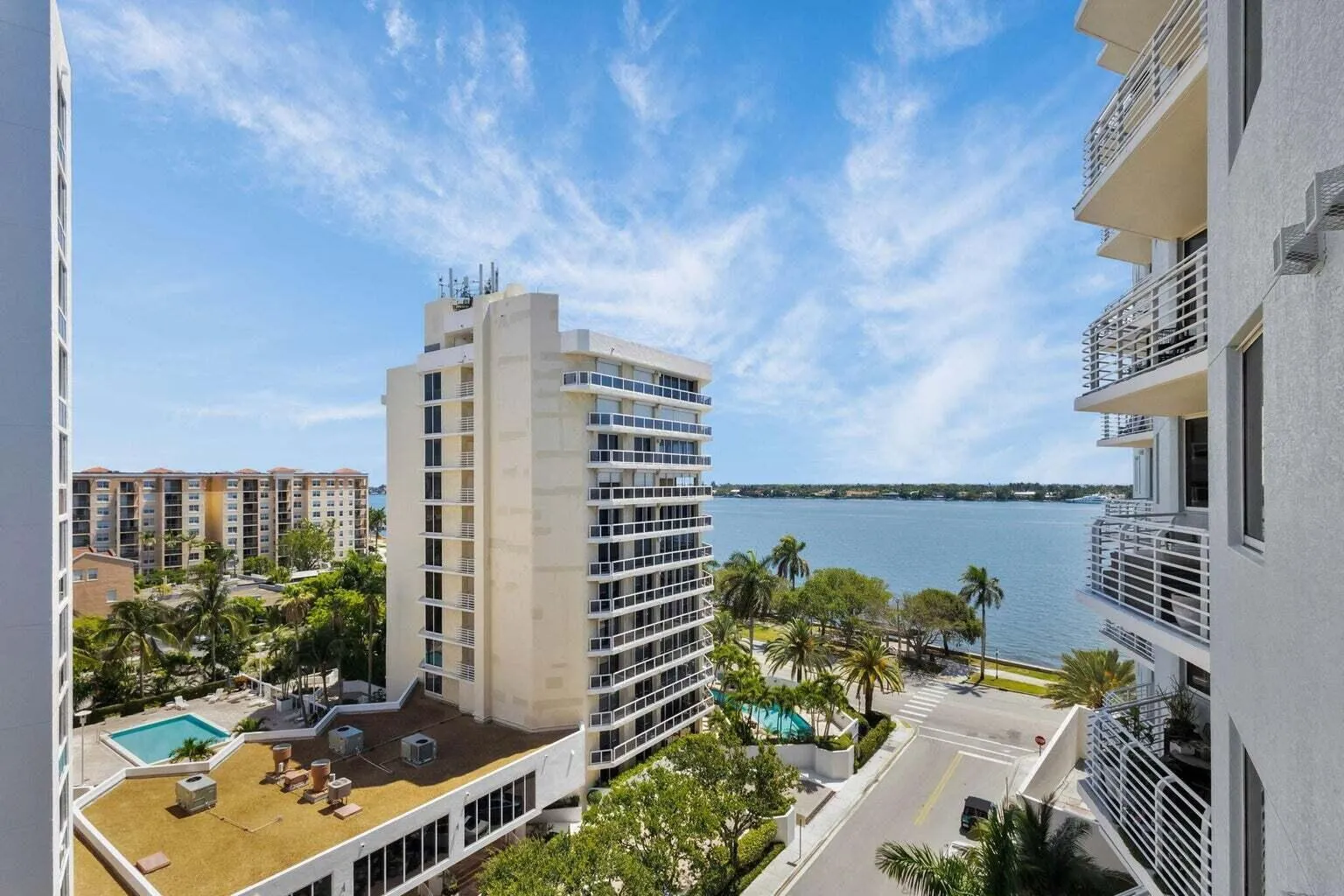 Waterfront panorama featuring high-rise architecture, lush palm trees, and a ground-level swimming pool