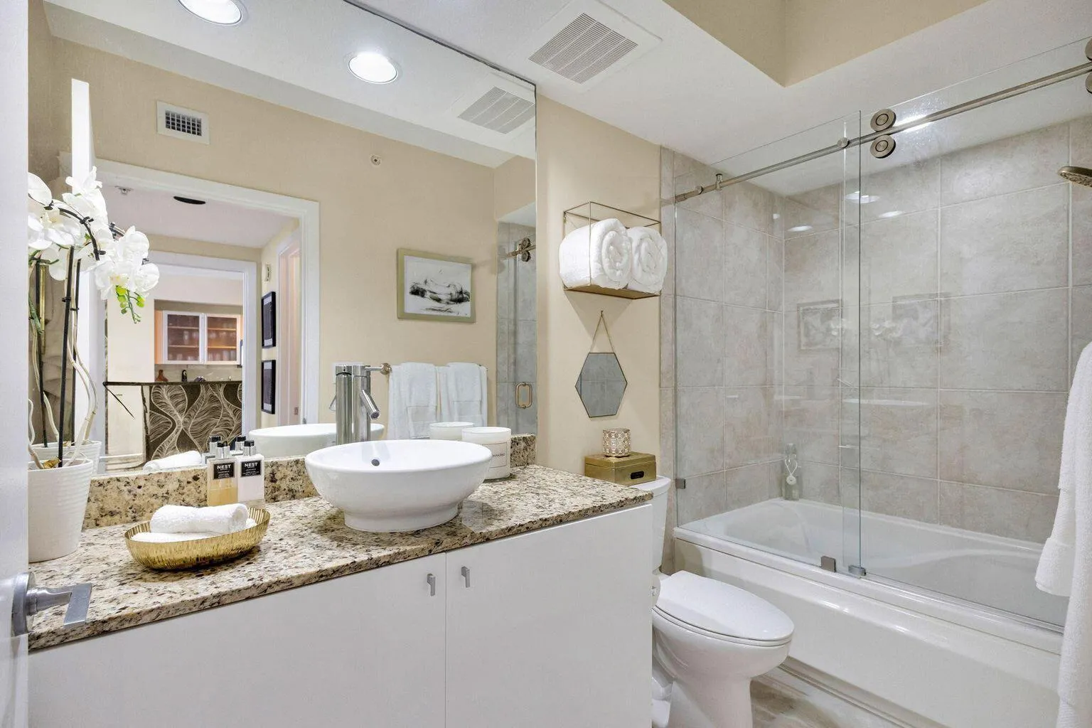 Bathroom featuring a vessel sink atop a granite-look countertop, white cabinetry, and a full-size tub with sliding glass doors