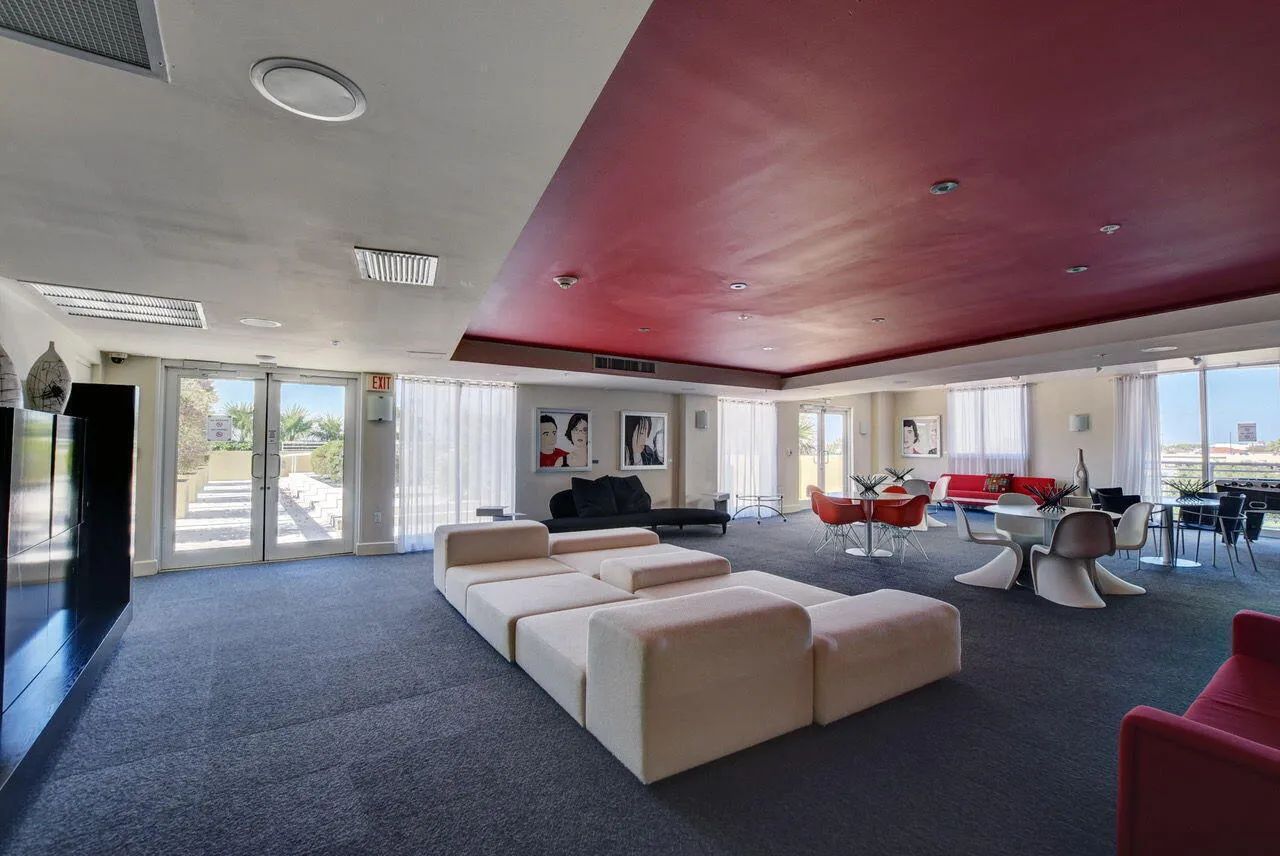 Spacious interior with dark gray carpet flooring, a partial red ceiling accent, and large windows with white sheer curtains