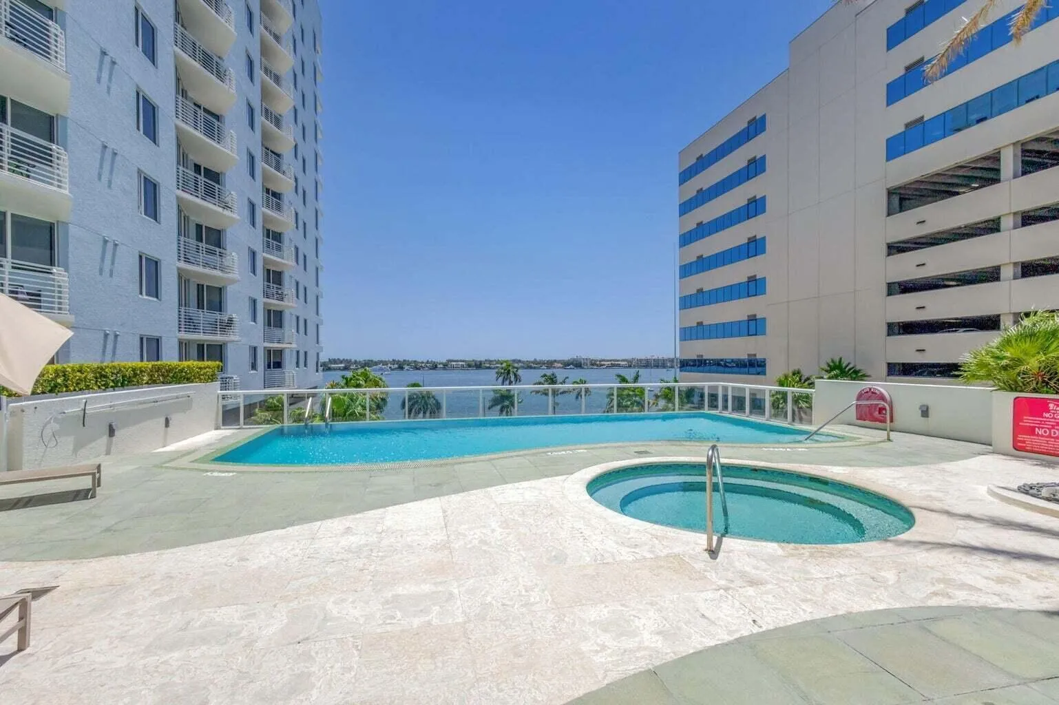Resort-style pool deck featuring a swimming pool, integrated spa, and water backdrop