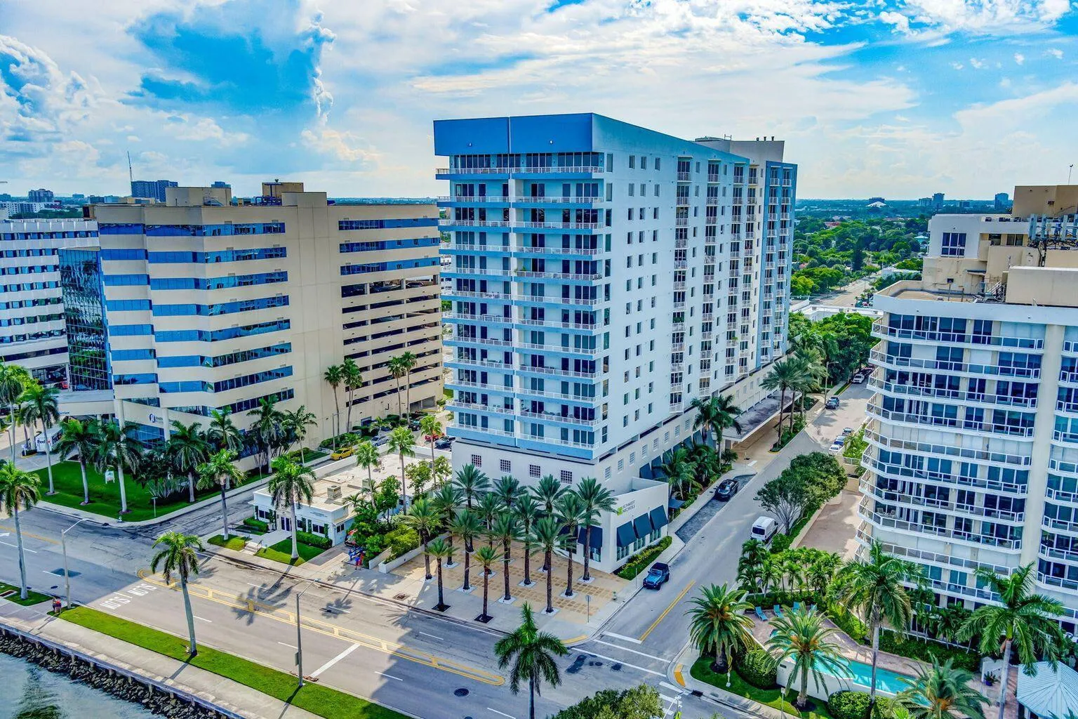 Multi-story building featuring multiple private balconies, a ground-level covered entry, and extensive perimeter landscaping with palm trees