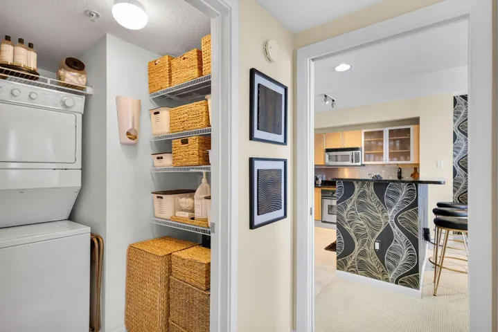 Dedicated laundry closet featuring a stacked washer and dryer, wire shelving, and overhead lighting