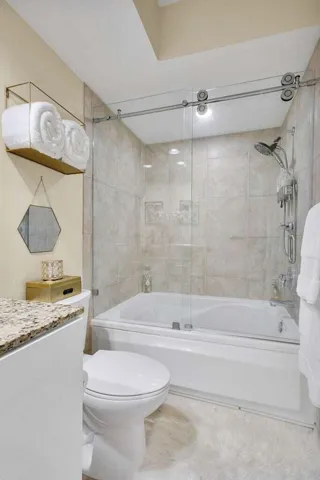 Bathroom featuring a spacious soaking tub with a glass sliding shower enclosure, a stone-finish countertop, tiled shower walls, and a recessed ceiling light