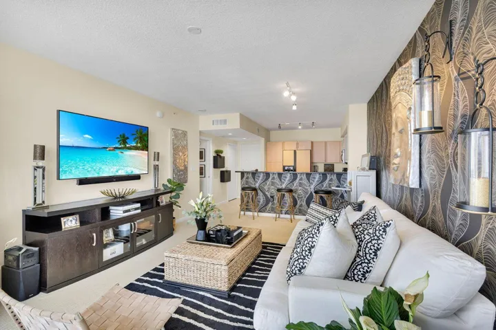 Open concept living area featuring a neutral color palette, accent wall with decorative sconces, recessed lighting, and a breakfast bar with countertop seating