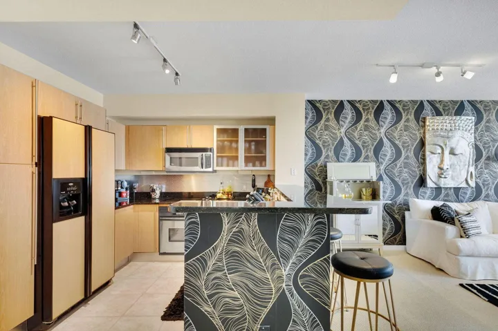 Open-concept living space with a kitchen featuring light wood-finish cabinetry and stainless steel appliances