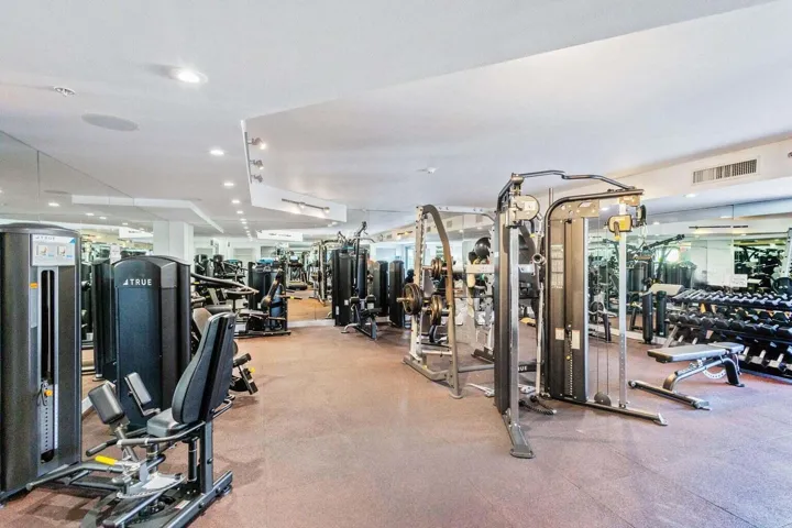 Equipped fitness center featuring various strength training machines, free weights, mirrored walls, recessed lighting, and a durable floor surface