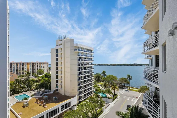 Waterfront panorama featuring high-rise architecture, lush palm trees, and a ground-level swimming pool