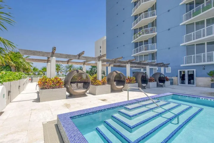 Outdoor patio area featuring a tiled pool with steps, a wood pergola structure, and multiple seating pods