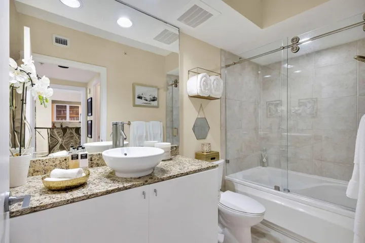 Bathroom featuring a vessel sink atop a granite-look countertop, white cabinetry, and a full-size tub with sliding glass doors