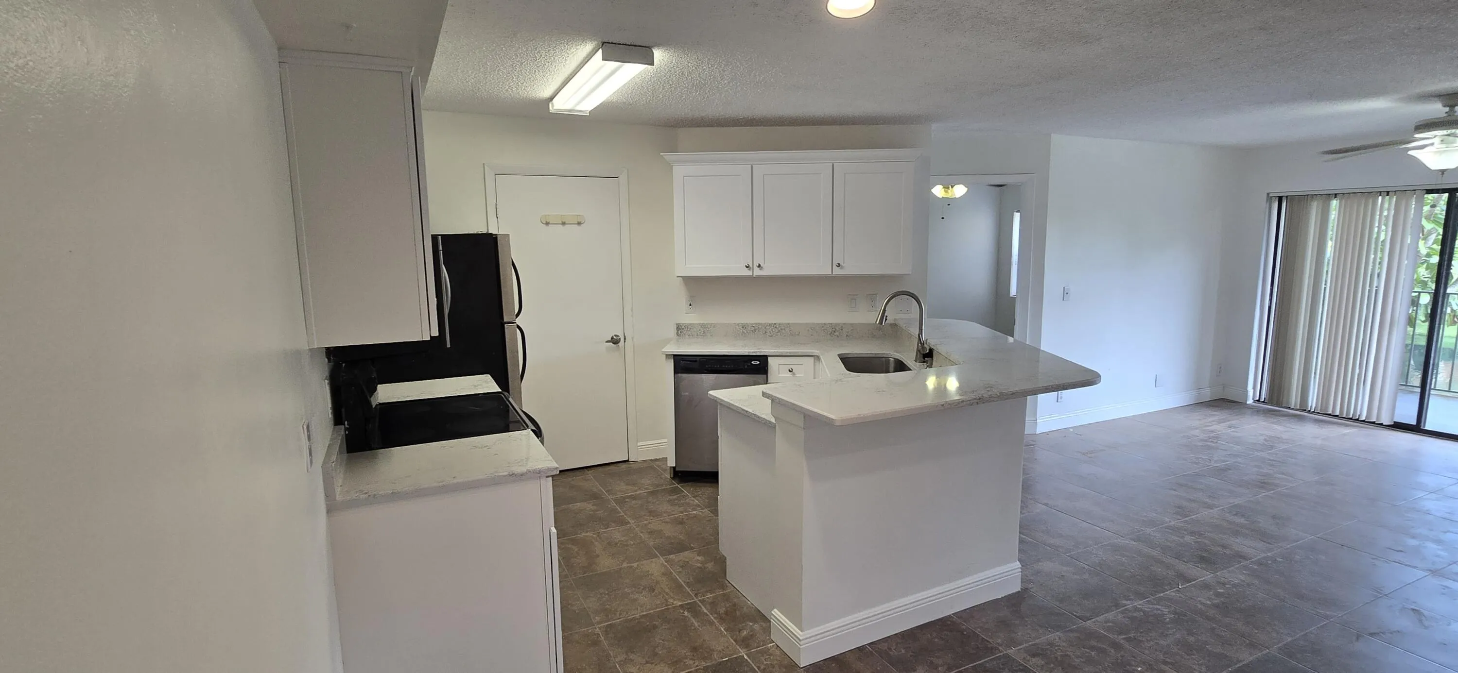 Open-concept kitchen and living area featuring a white cabinetry kitchen with stainless steel appliances, a large center island with waterfall countertop, and wood-finish flooring throughout