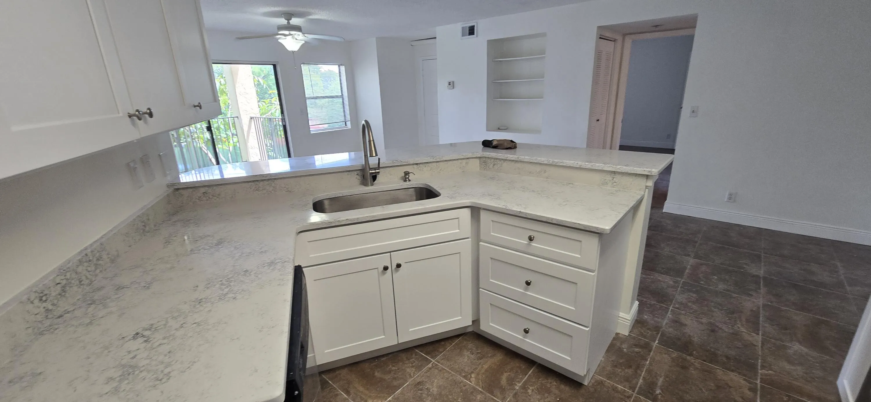 Bright kitchen featuring white cabinetry, stone countertops with waterfall edge detailing, stainless steel sink, and an island layout