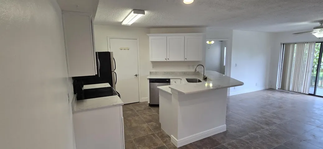 Open-concept kitchen and living area featuring a white cabinetry kitchen with stainless steel appliances, a large center island with waterfall countertop, and wood-finish flooring throughout