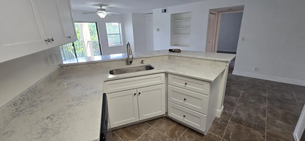 Bright kitchen featuring white cabinetry, stone countertops with waterfall edge detailing, stainless steel sink, and an island layout