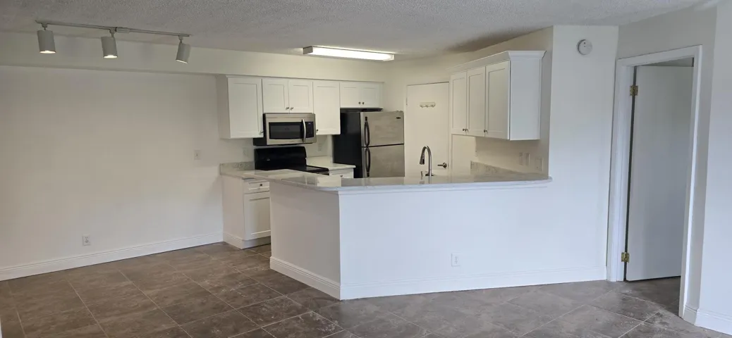 Open-concept kitchen featuring white cabinetry, stone-finish countertops, stainless steel appliances, and a breakfast bar