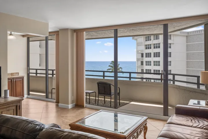 Expansive oceanfront living room showcasing floor-to-ceiling sliding glass doors, wood-finish flooring, and a private balcony with unobstructed water
