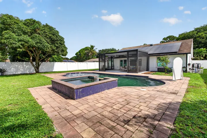 Backyard oasis featuring an inground pool, integrated spa with blue tile accents, and an expansive paver patio