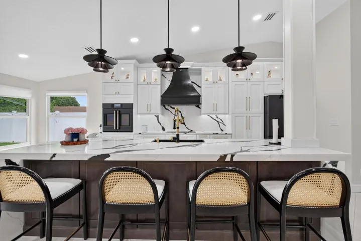 Modern kitchen featuring a large island with waterfall-edge countertop, white shaker-style cabinetry, and integrated black appliances