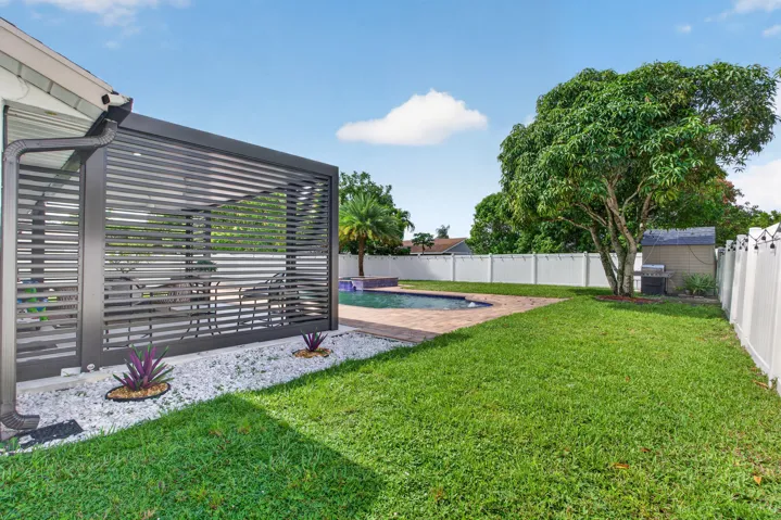 Backyard featuring a modern louvered pergola, a swimming pool with paver surround, a spacious lawn, a mature tree, and a white privacy fence