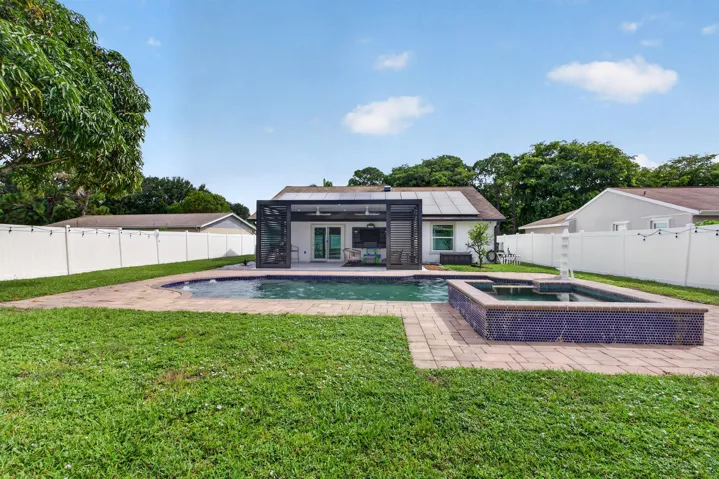 Modern residence showcasing a resort-style backyard oasis featuring a sparkling swimming pool with integrated spa, brick paver surround, manicured lawn, black-framed architectural design with contemporary finishes, mature landscaping, and white privacy fencing