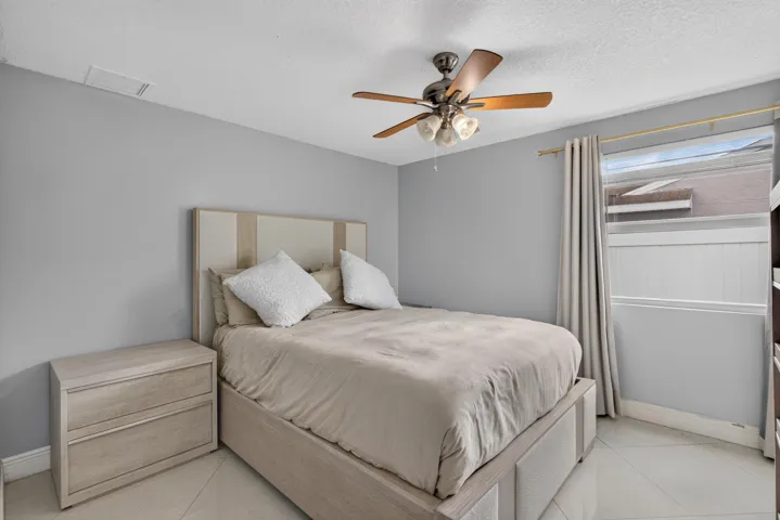 Bedroom featuring light gray walls, a window with curtains, and a ceiling fan with light fixture
