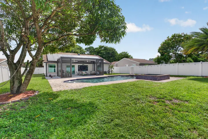 Spacious backyard featuring an in-ground swimming pool with an integrated spa, a screened patio enclosure, and a paved pool deck