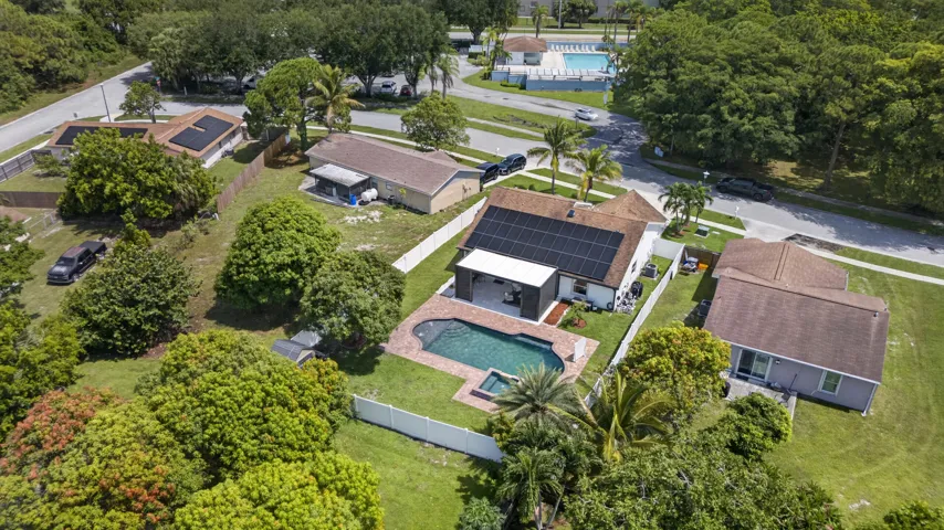 Aerial view showcasing a contemporary home with a resort-style backyard featuring an in-ground swimming pool, expansive manicured lawn, mature landscaping, and multiple outbuildings