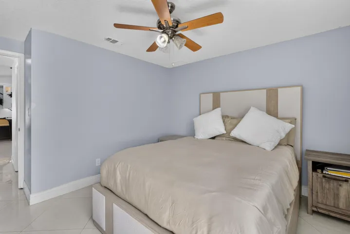 Bedroom featuring light blue walls, white baseboards, and a ceiling fan with wood-finish blades