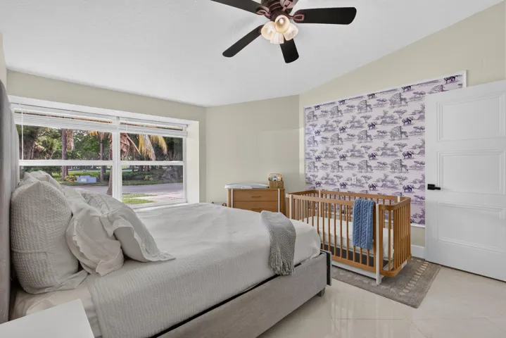 Bright bedroom featuring large windows, light-toned walls, a modern ceiling fan, and a white paneled door
