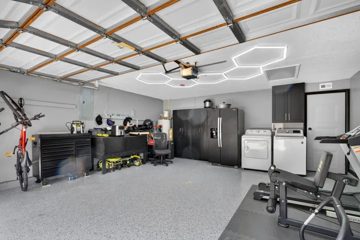Spacious garage featuring a durable epoxy floor, contemporary ceiling lighting, painted walls, wall-mounted cabinetry, and a dedicated laundry area with washer and dryer