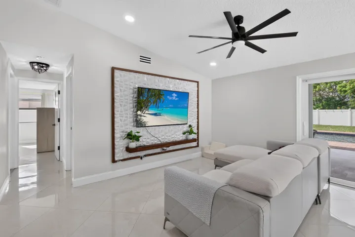 Expansive living area featuring large format tile flooring, a contemporary ceiling fan, recessed lighting, and a built-in media wall with a wood-finish frame