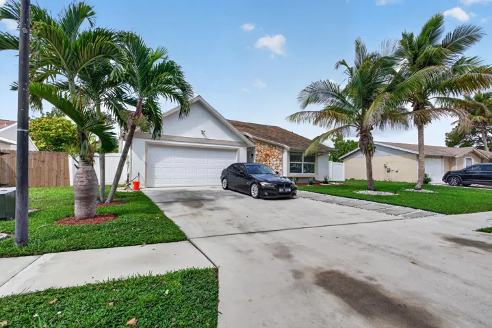 Single-story residence featuring a white garage door, stone and stucco exterior, and a manicured front lawn with mature palm trees