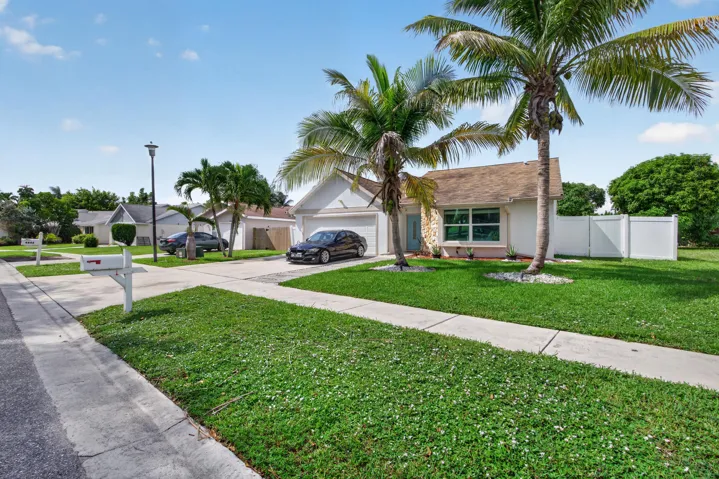 Single-story residence featuring a two-car garage, white privacy fence, two mature palm trees, and a stone facade accent