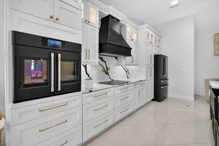 Modern kitchen featuring white shaker cabinetry with brass hardware, black built-in oven, black range hood, and black refrigerator