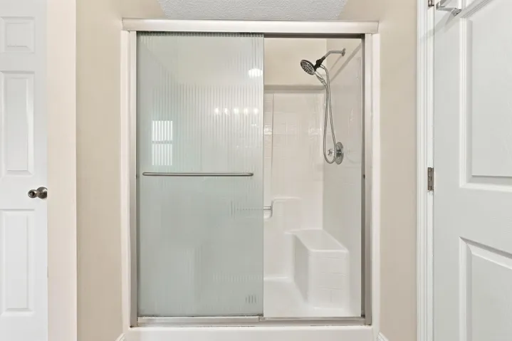 Enclosed shower featuring clear and frosted glass panels with a chrome frame, chrome shower fixtures, and an integrated shower bench