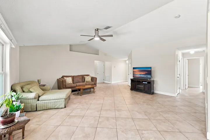 Expansive living area featuring light-toned tile flooring, vaulted ceilings, a ceiling fan, and ample natural light from large windows