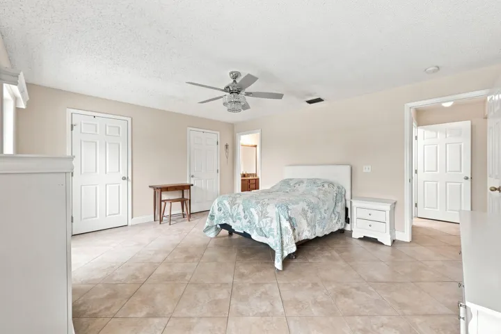 Spacious room featuring neutral-toned tile flooring, light beige walls, multiple paneled doors, and a ceiling fan with integrated lighting