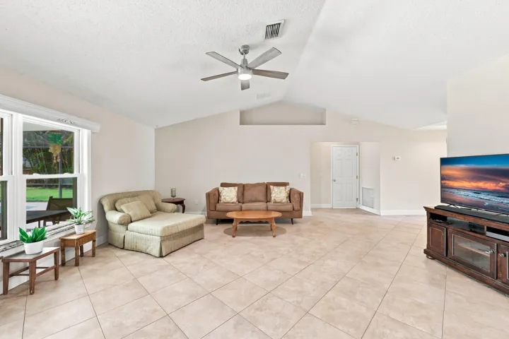 Spacious living area featuring large-format tile flooring, vaulted ceilings, and a ceiling fan