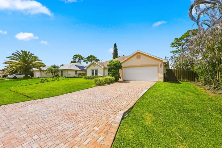 Front exterior featuring a cream-colored stucco finish, a two-car garage with a white door, and a brick paver driveway